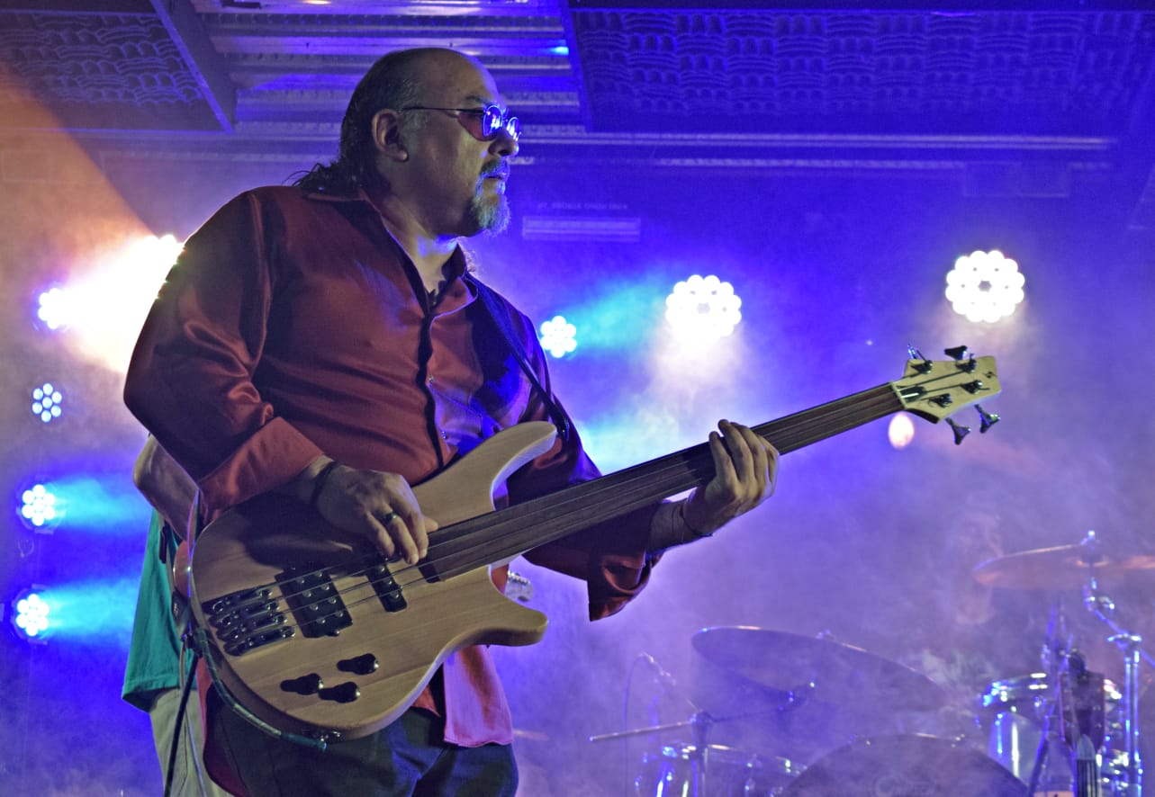 Portrait of Alex Jara holding a bass guitar in blue stage haze